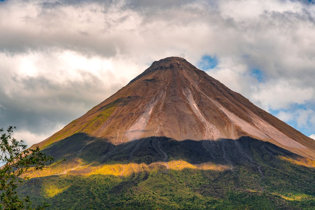 Arenal Volcano's conical peak rises above forested slopes under partly cloudy skies in Costa Rica.